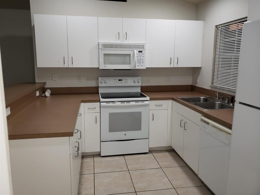 A kitchen features white cabinets, brown countertops, white appliances, and light-colored tile flooring — 2209/2211 DANIEL AVENUE N, LEHIGH ACRES, FL