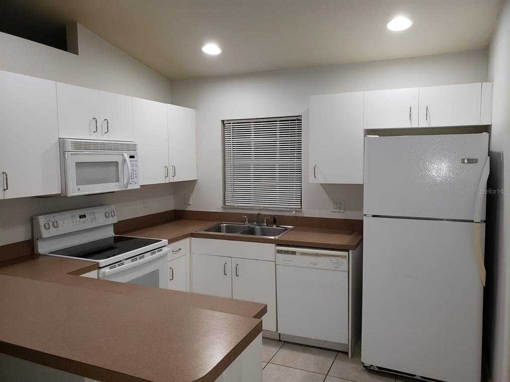 A kitchen with white cabinets, brown countertops, white appliances, and a window with blinds — 2209/2211 DANIEL AVENUE N, LEHIGH ACRES, FL