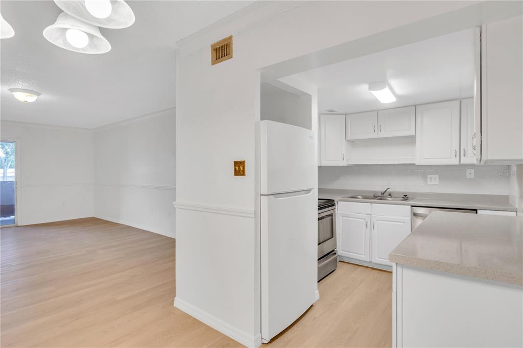 A kitchen with white cabinets and a refrigerator opens into a light-floored living area — 916 LAKE DESTINY ROAD UNIT E, ALTAMONTE SPRINGS, FL