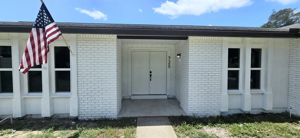 A white brick exterior features a double front door and an American flag — 725 TULIP COURT, DELTONA, FL