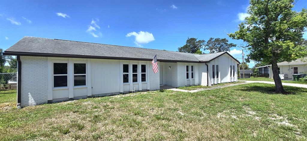 A single-story white brick house with a gray shingled roof and an American flag — 725 TULIP COURT, DELTONA, FL