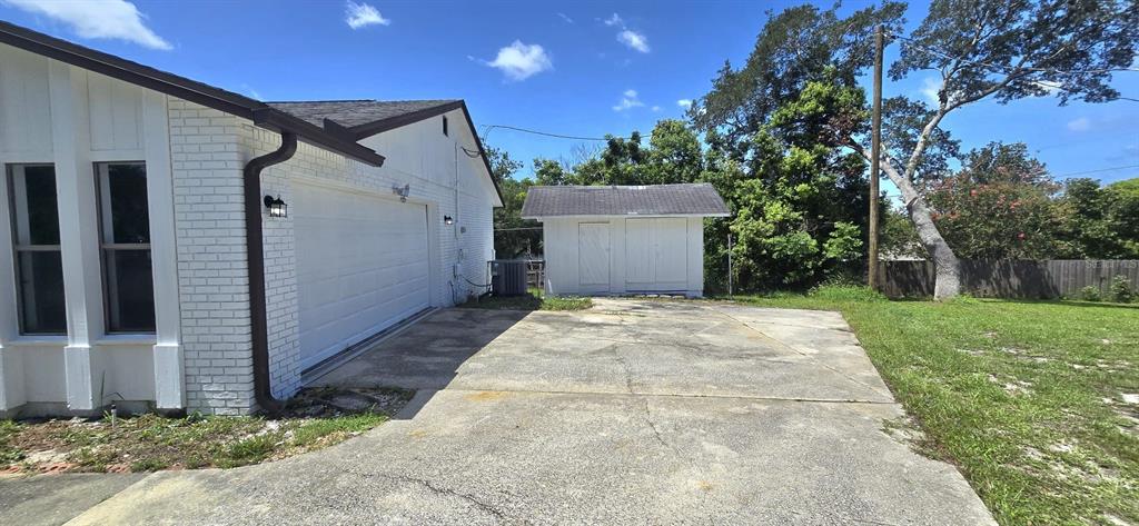 A white brick house with a garage and a detached shed on a concrete driveway — 725 TULIP COURT, DELTONA, FL
