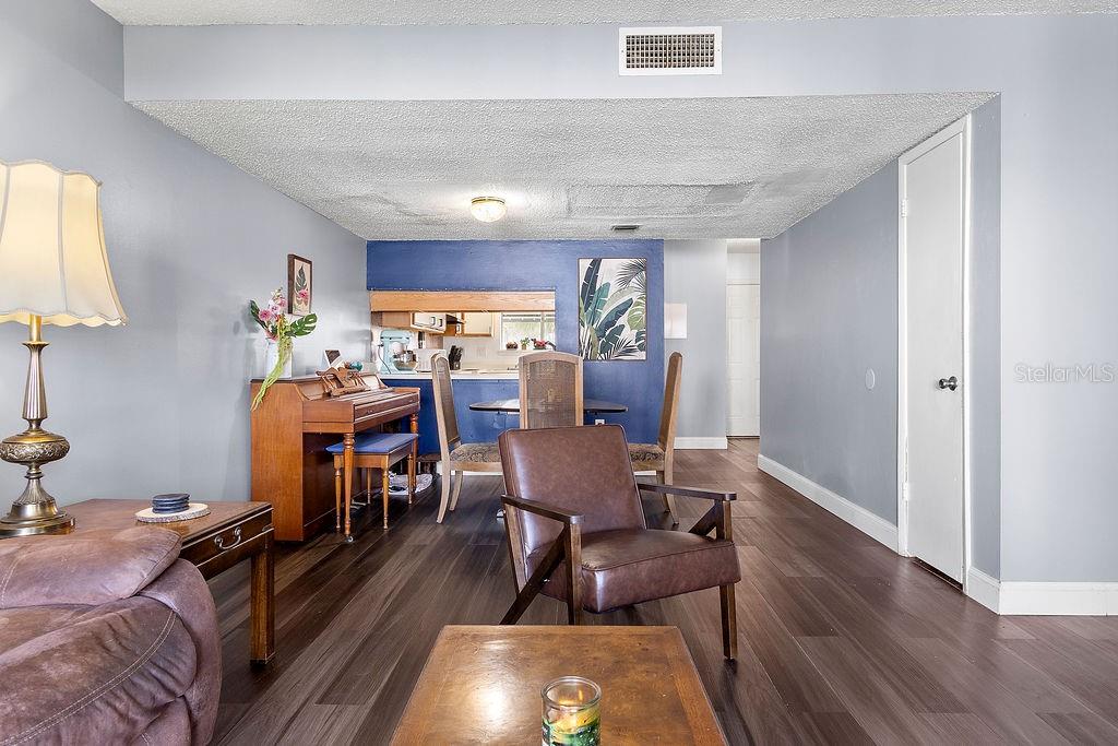 A living and dining area features dark wood-look flooring, blue accent walls, and a piano — 4269 S SEMORAN BOULEVARD UNIT 14, ORLANDO, FL