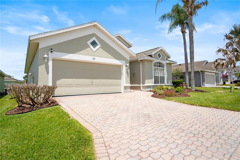 A single-story house with a beige stucco exterior, a two-car garage, and a paver driveway — 223 RIDGE VIEW DRIVE, DAVENPORT, FL