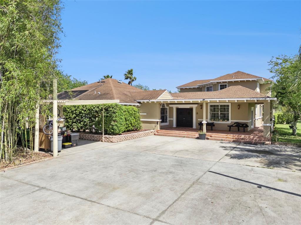 A tan house with a brown shingled roof features a large concrete driveway and porch — 5825 LAKE LIZZIE DRIVE, ST CLOUD, FL