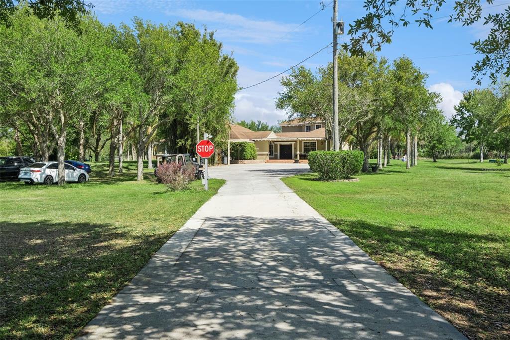 A long concrete driveway leads to a two-story house surrounded by trees and green lawns — 5825 LAKE LIZZIE DRIVE, ST CLOUD, FL