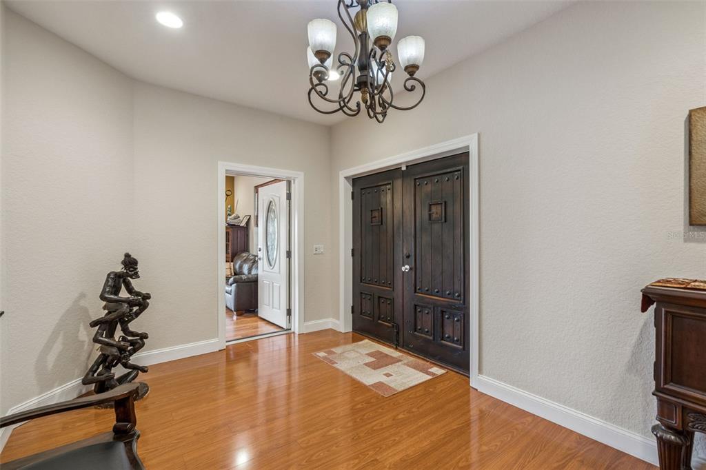 An entryway features hardwood floors, a chandelier, and dark wood double doors — 5825 LAKE LIZZIE DRIVE, ST CLOUD, FL