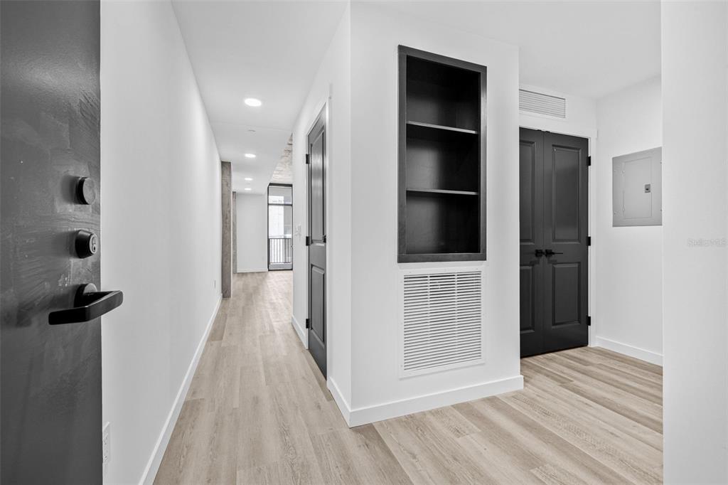 A hallway with light wood-look flooring, black doors, a built-in shelf, and recessed lighting — 221 MAIN STREET N UNIT A2-1102, ST PETERSBURG, FL