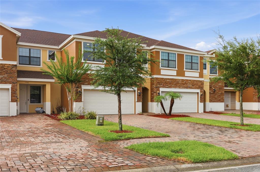 A row of two-story townhomes with stone facades, brick paver driveways, and attached garages — 1940 PORTOFINO MEADOWS BOULEVARD, ORLANDO, FL
