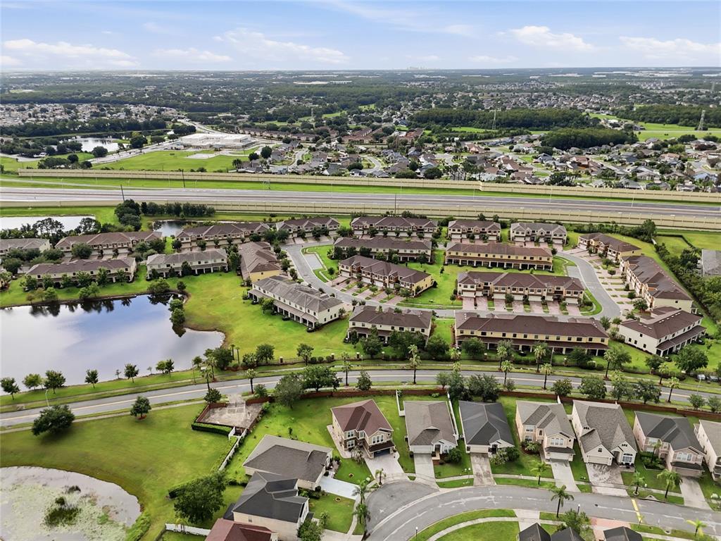 An aerial view shows a suburban neighborhood with townhomes, single-family houses, and a retention pond — 1940 PORTOFINO MEADOWS BOULEVARD, ORLANDO, FL