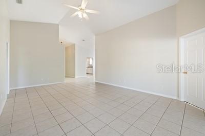 A spacious, empty living room features light-colored tile flooring, vaulted ceilings, and a ceiling fan — 3865 OSPREY POINTE CIRCLE, WINTER HAVEN, FL