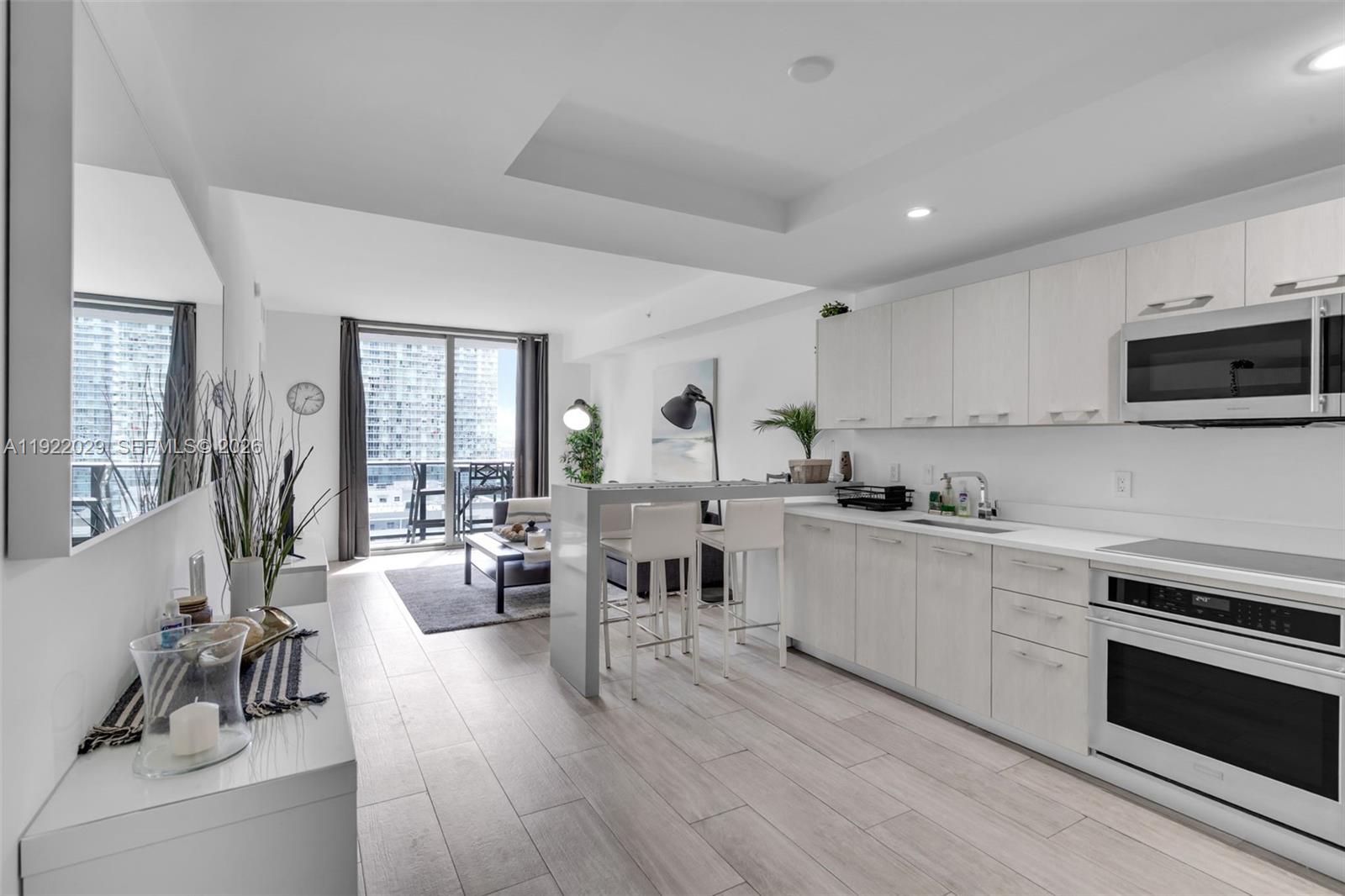 A modern kitchen with light wood cabinets and a breakfast bar opens to a living area — 55 SW 9th St # 1705, Miami FL 33130, MIAMI, FL