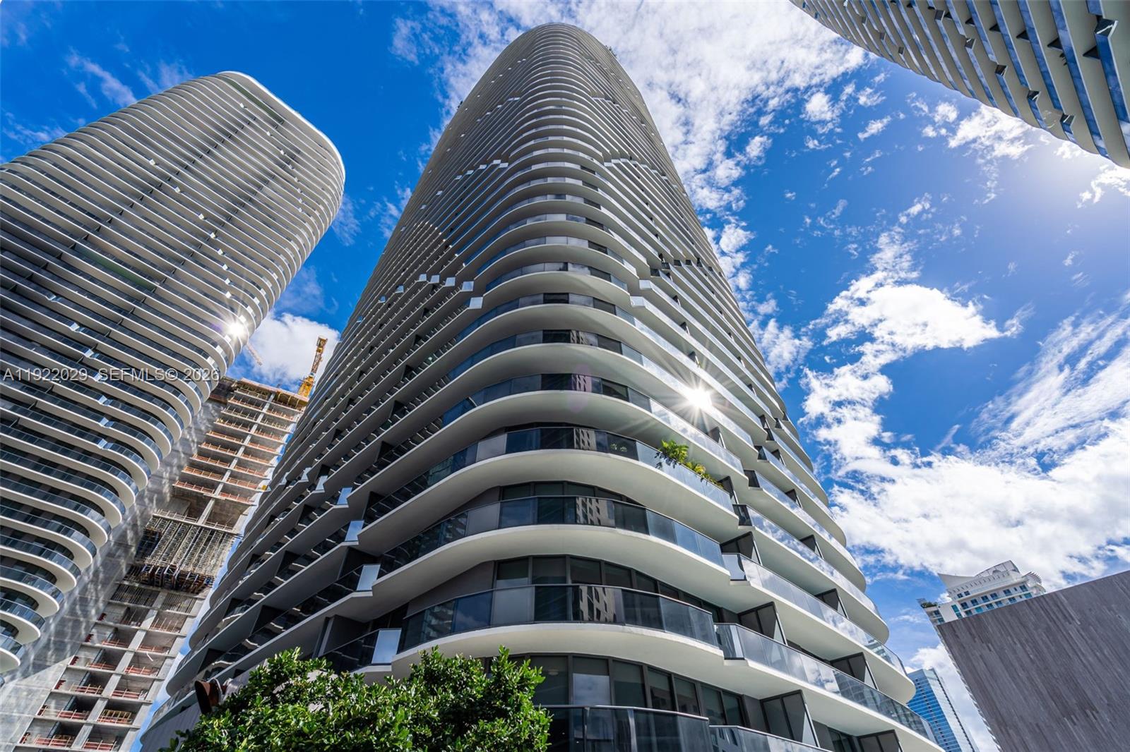 A low-angle view shows the curved, white-balconied exterior of a modern high-rise residential building — 55 SW 9th St # 1705, Miami FL 33130, MIAMI, FL