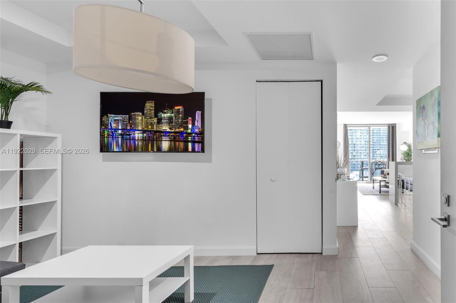 A white living room features a wall-mounted television, a bookshelf, and a closet door — 55 SW 9th St # 1705, Miami FL 33130, MIAMI, FL