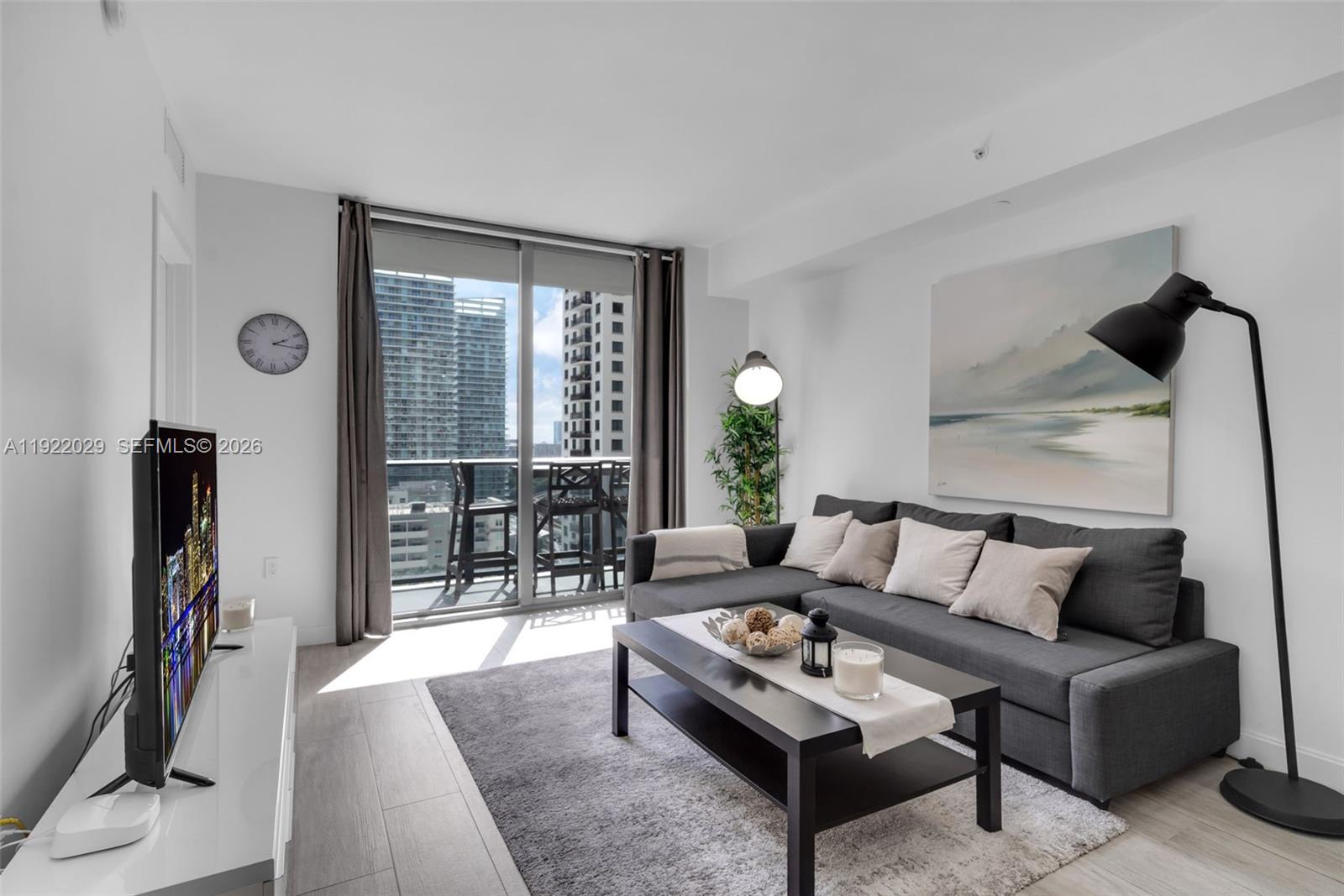 A modern living room features a gray sectional sofa, coffee table, and balcony access — 55 SW 9th St # 1705, Miami FL 33130, MIAMI, FL