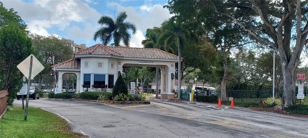 A gated community entrance features a guardhouse with a tile roof and palm trees — 1000 SAINT CHARLES PLACE UNIT 209, PEMBROKE PINES, FL