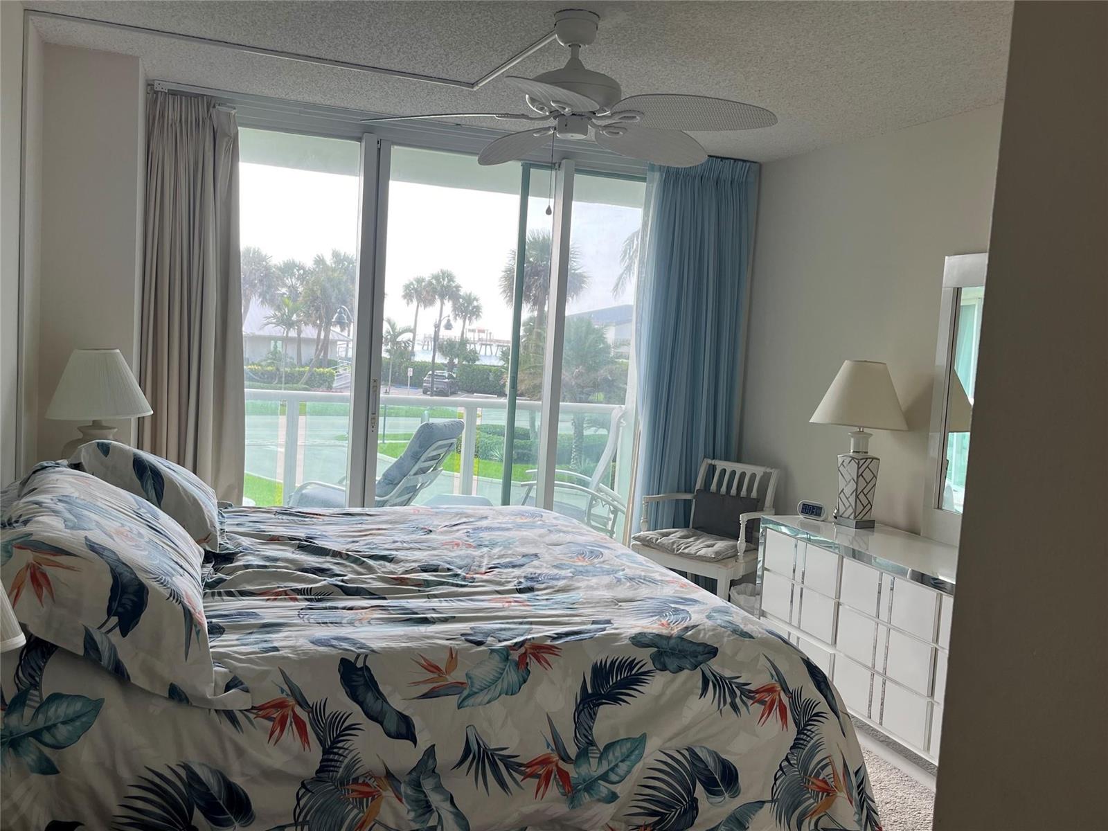 A bedroom features a tropical print comforter, a ceiling fan, and sliding doors to a balcony — 333 NE 21st Avenue # 318, Deerfield Beach FL 33441, DEERFIELD BEACH, FL