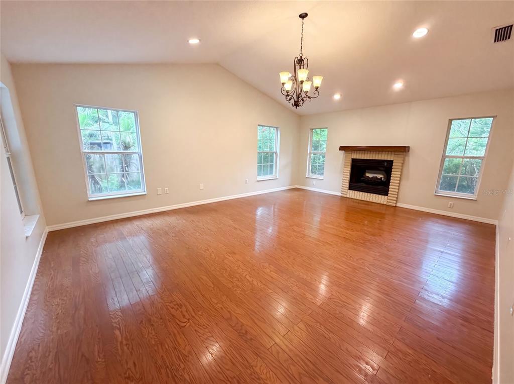 A spacious living room features hardwood floors, a vaulted ceiling, a chandelier, and a fireplace — 11540 CAMP DRIVE, DUNNELLON, FL