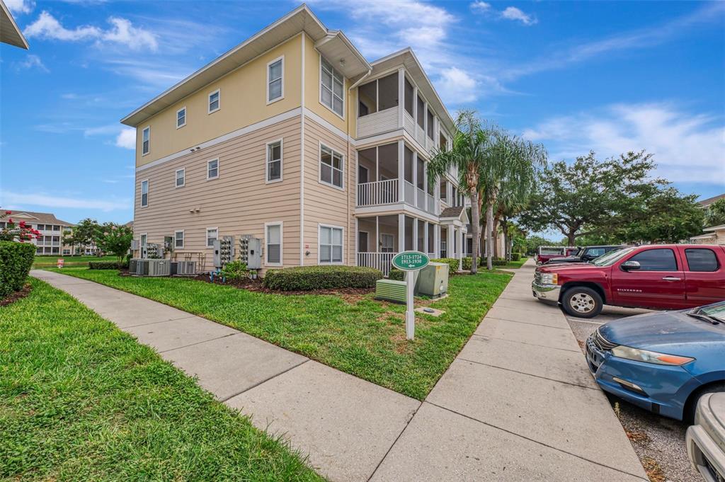 A three-story apartment building with beige siding and screened balconies sits beside a parking lot — 4802 51ST STREET W UNIT 1903, BRADENTON, FL