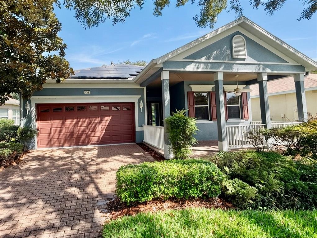 A single-story house with a brick driveway, blue siding, red shutters, and solar panels — 129 CREPE MYRTLE DRIVE, GROVELAND, FL