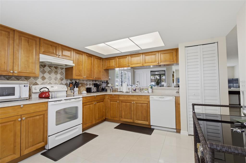 A kitchen features light wood cabinets, white appliances, a tiled backsplash, and beige floor tiles — 2701 COUNTRYSIDE BOULEVARD UNIT 101, CLEARWATER, FL