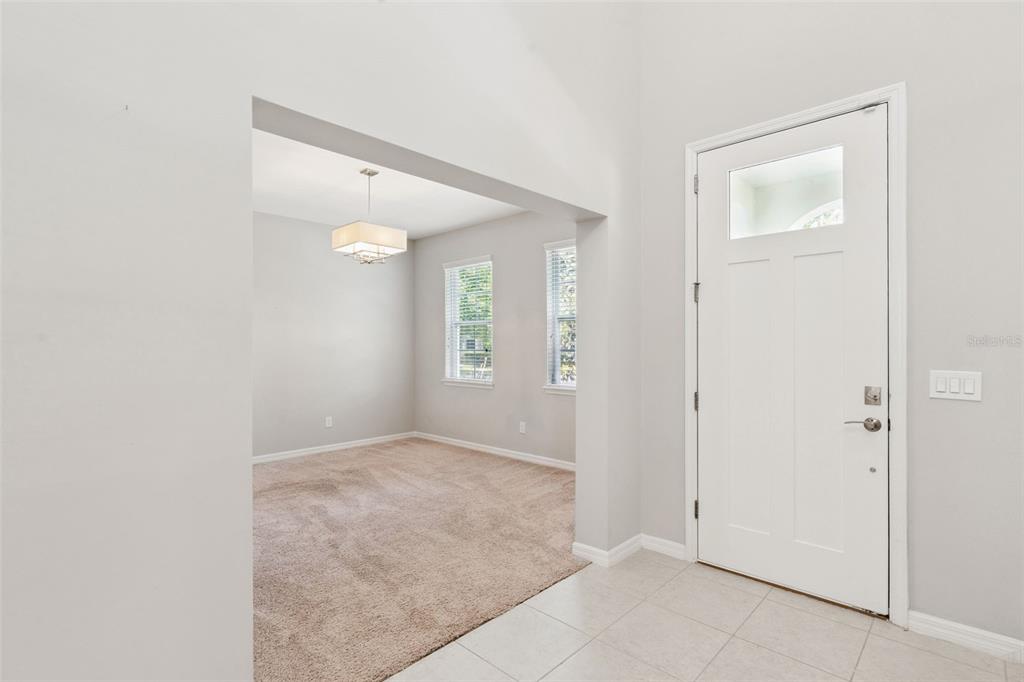 A tiled entryway leads to a carpeted dining room with a modern chandelier and windows — 14005 ALDFORD DRIVE, WINTER GARDEN, FL