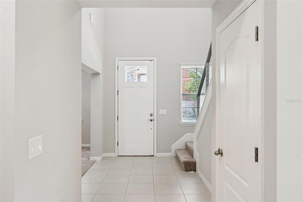 A bright entryway features light tile flooring, a white front door, and a carpeted staircase — 14005 ALDFORD DRIVE, WINTER GARDEN, FL