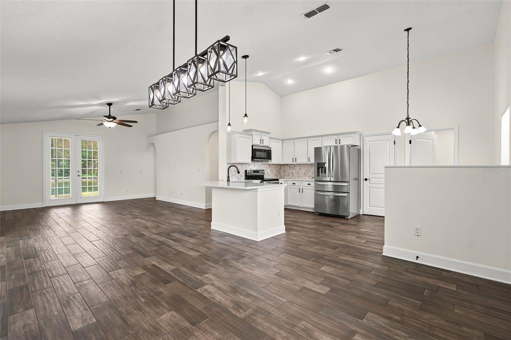 An open-concept kitchen and living area featuring white cabinetry, a center island, and wood-look flooring — 2608 DECK AVENUE, KISSIMMEE, FL