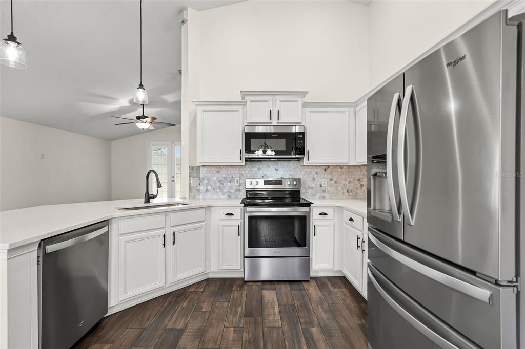 A kitchen features white cabinets, stainless steel appliances, a tiled backsplash, and dark wood flooring — 2608 DECK AVENUE, KISSIMMEE, FL
