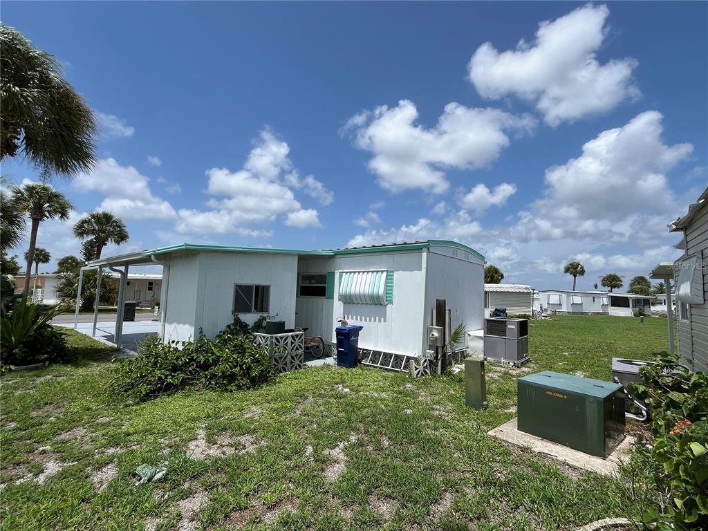 A white mobile home with a metal awning and a green utility box in the yard — 634 COMO DRIVE, VENICE, FL