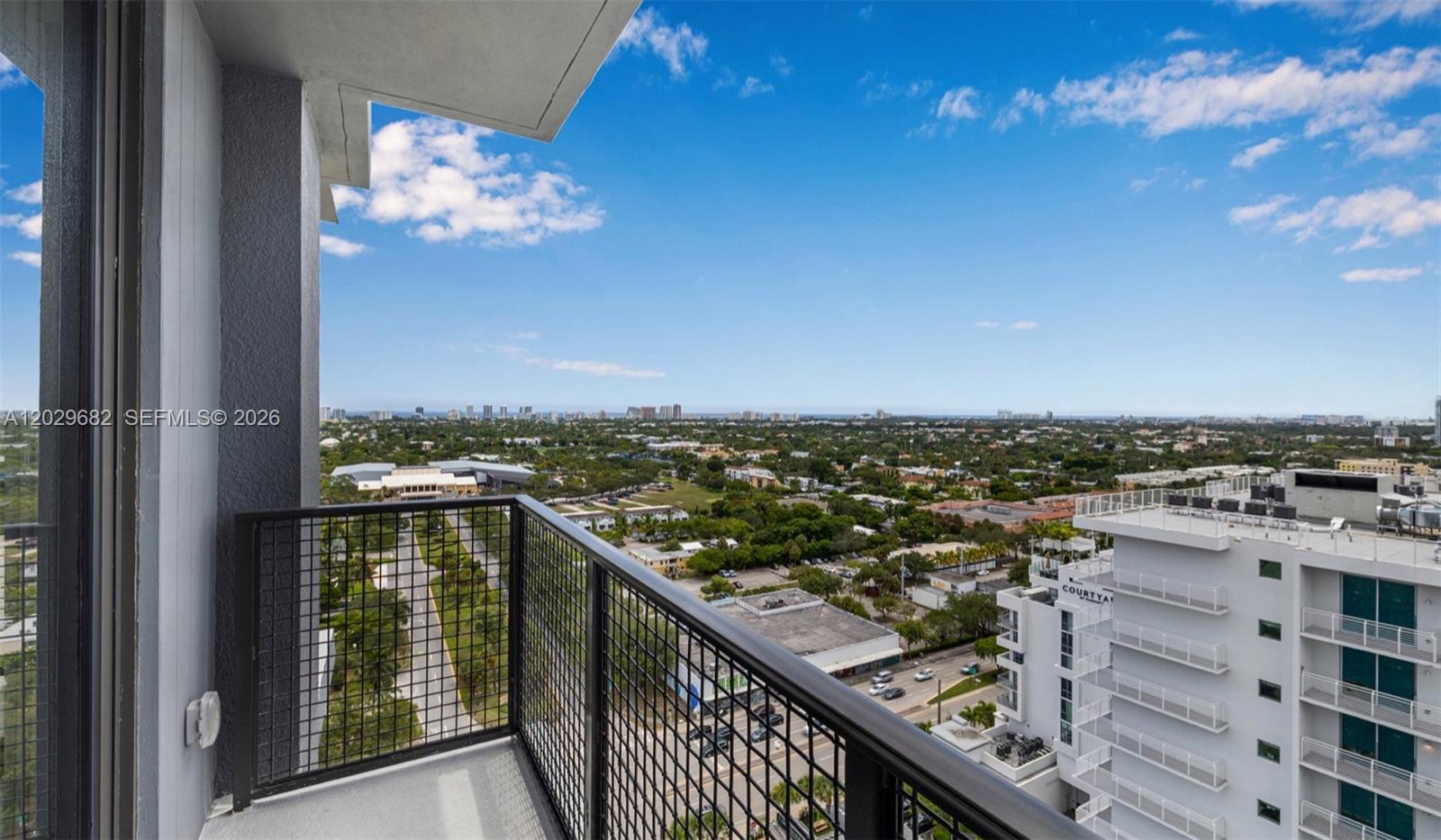 A high-rise balcony with a black metal railing overlooks a city and distant coastline — FORT LAUDERDALE, FL