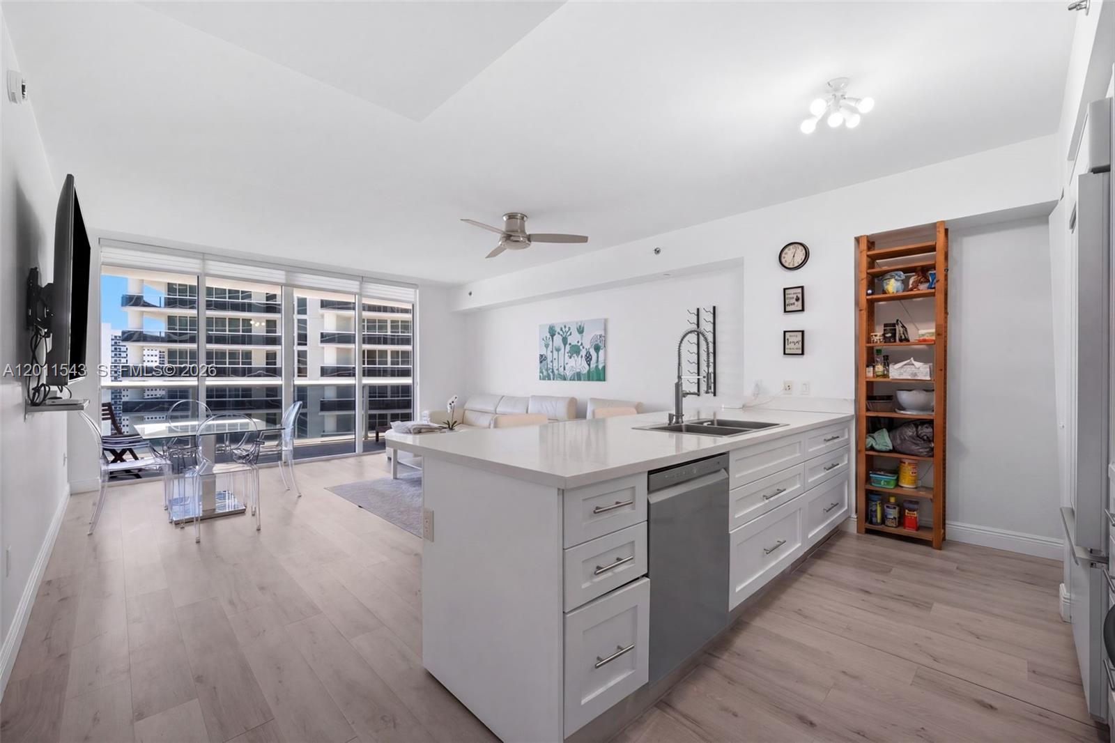 A modern kitchen with white cabinetry and an island overlooks a living area with balcony access — HALLANDALE BEACH, FL