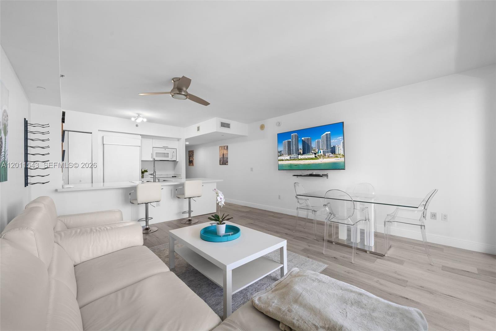 A modern living and dining area features white furniture, a glass table, and light flooring — HALLANDALE BEACH, FL