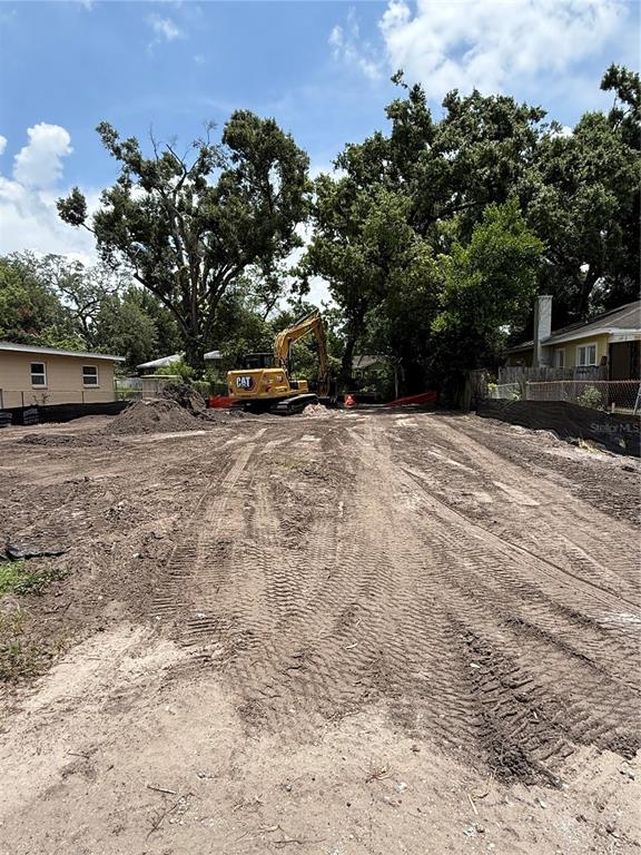 A yellow excavator sits on a cleared, dirt construction lot with surrounding trees and houses — 2711 N MYRTLE AVENUE, TAMPA, FL