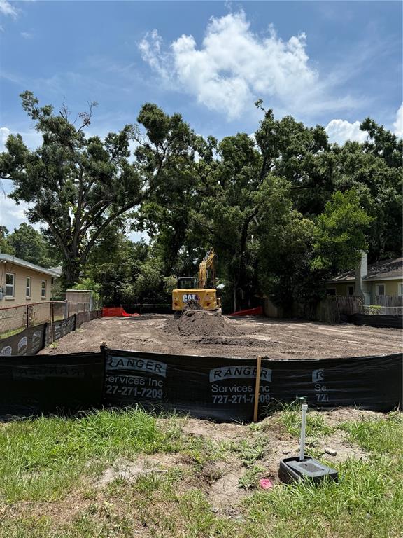A yellow excavator sits on a cleared, fenced construction lot with surrounding trees — 2711 N MYRTLE AVENUE, TAMPA, FL