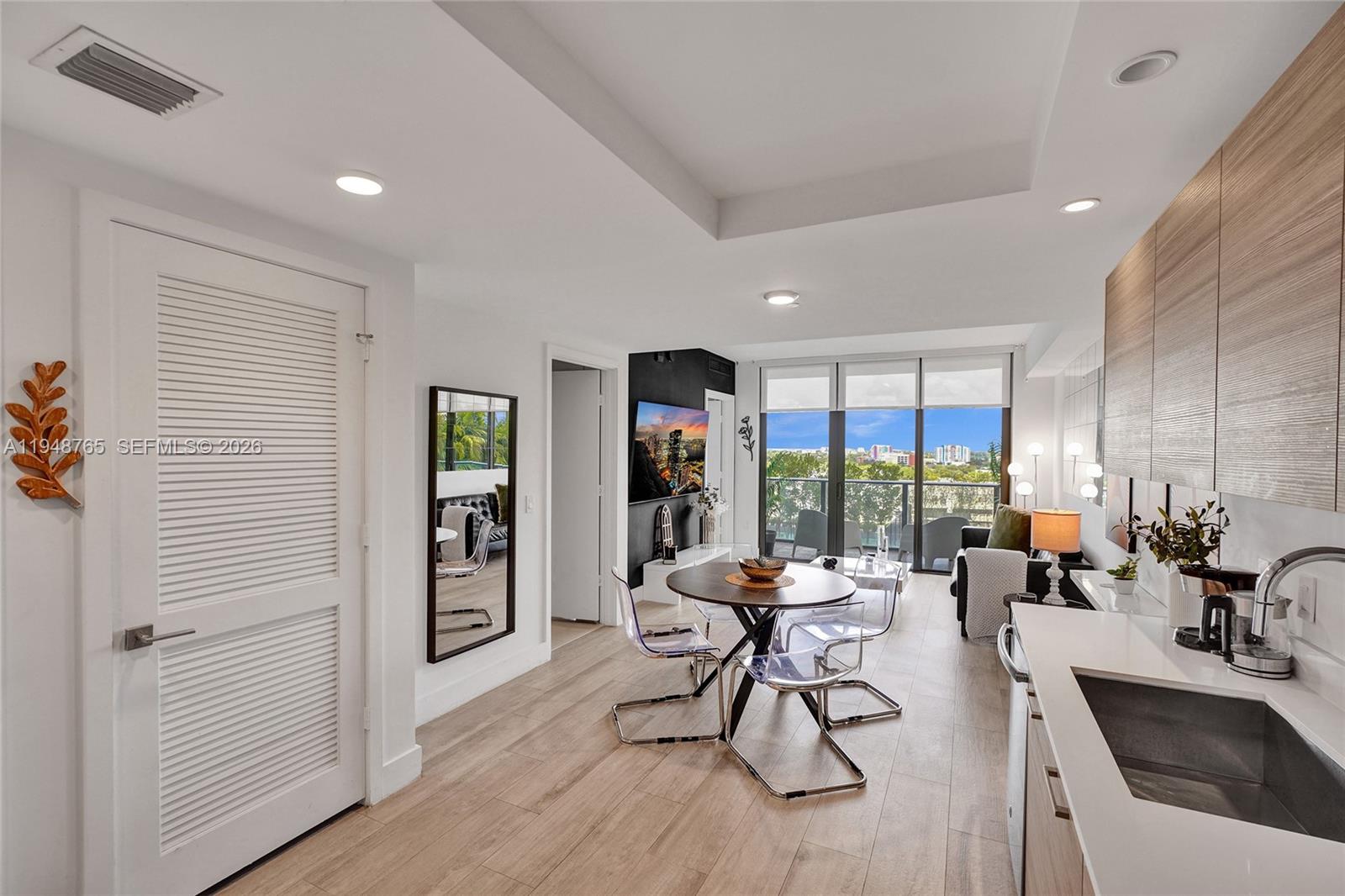 A modern open-concept living and dining area features a kitchen, balcony, and light wood flooring — 121 NE 34th St # 910, Miami FL 33137, MIAMI, FL