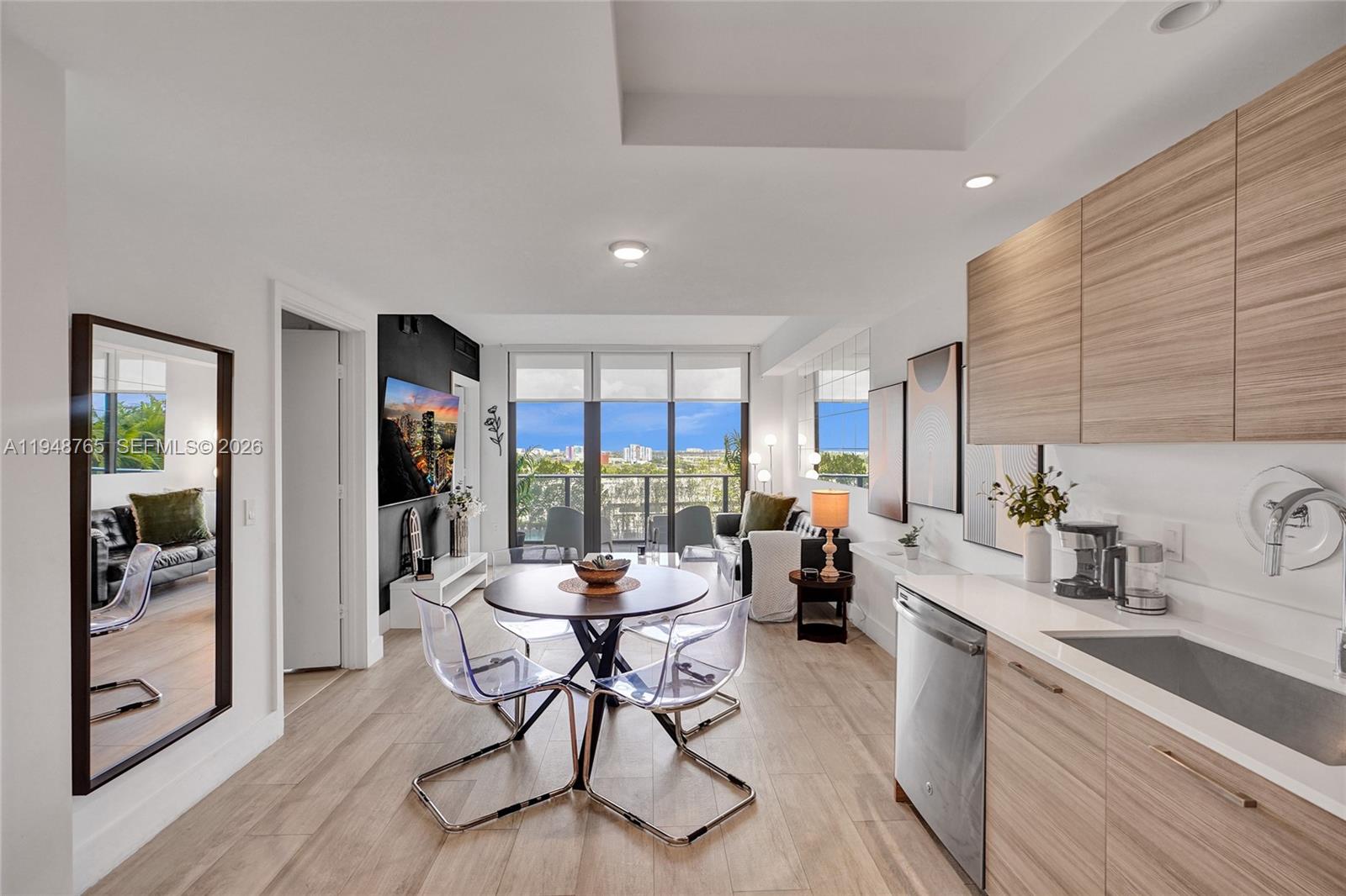 A modern kitchen and dining area features light wood cabinets, clear chairs, and balcony views — 121 NE 34th St # 910, Miami FL 33137, MIAMI, FL