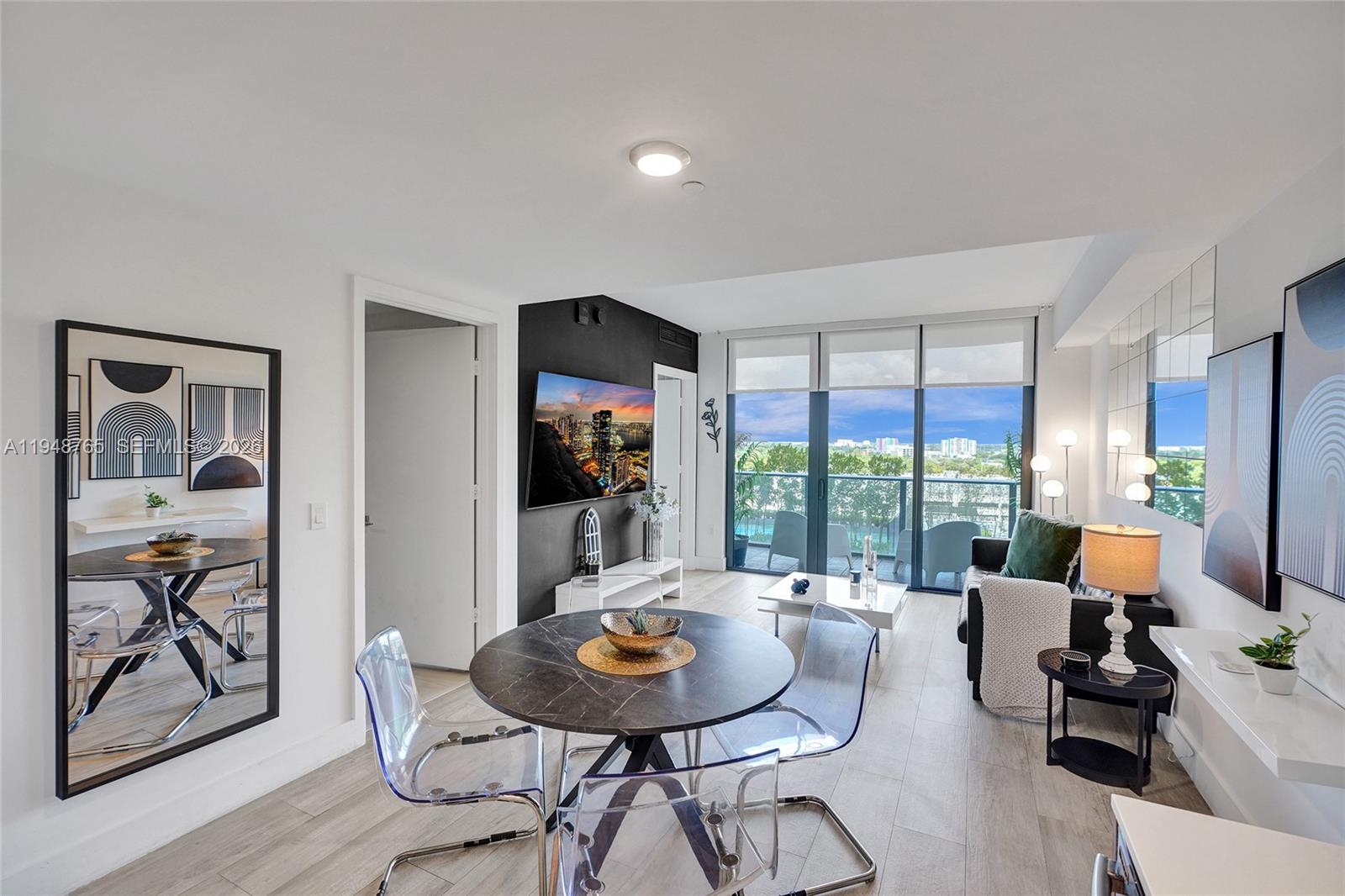 A modern living and dining area features a dark accent wall, balcony, and transparent chairs — 121 NE 34th St # 910, Miami FL 33137, MIAMI, FL