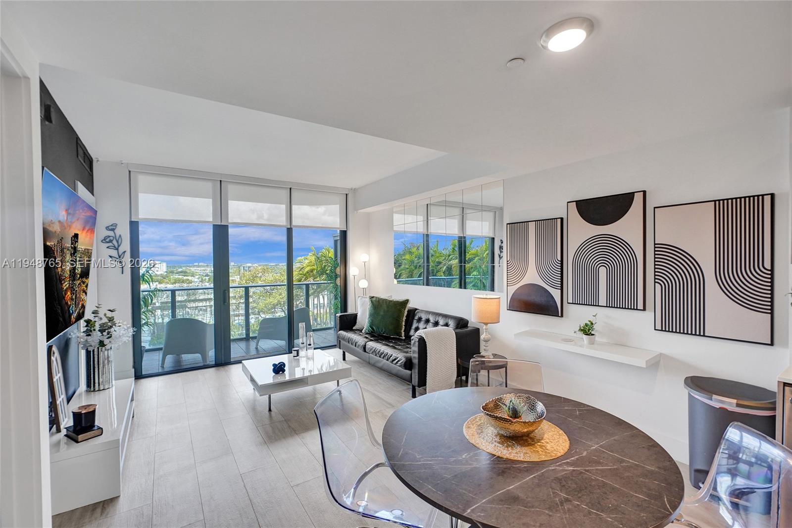 A modern living and dining area features a balcony, black leather sofa, and marble table — 121 NE 34th St # 910, Miami FL 33137, MIAMI, FL