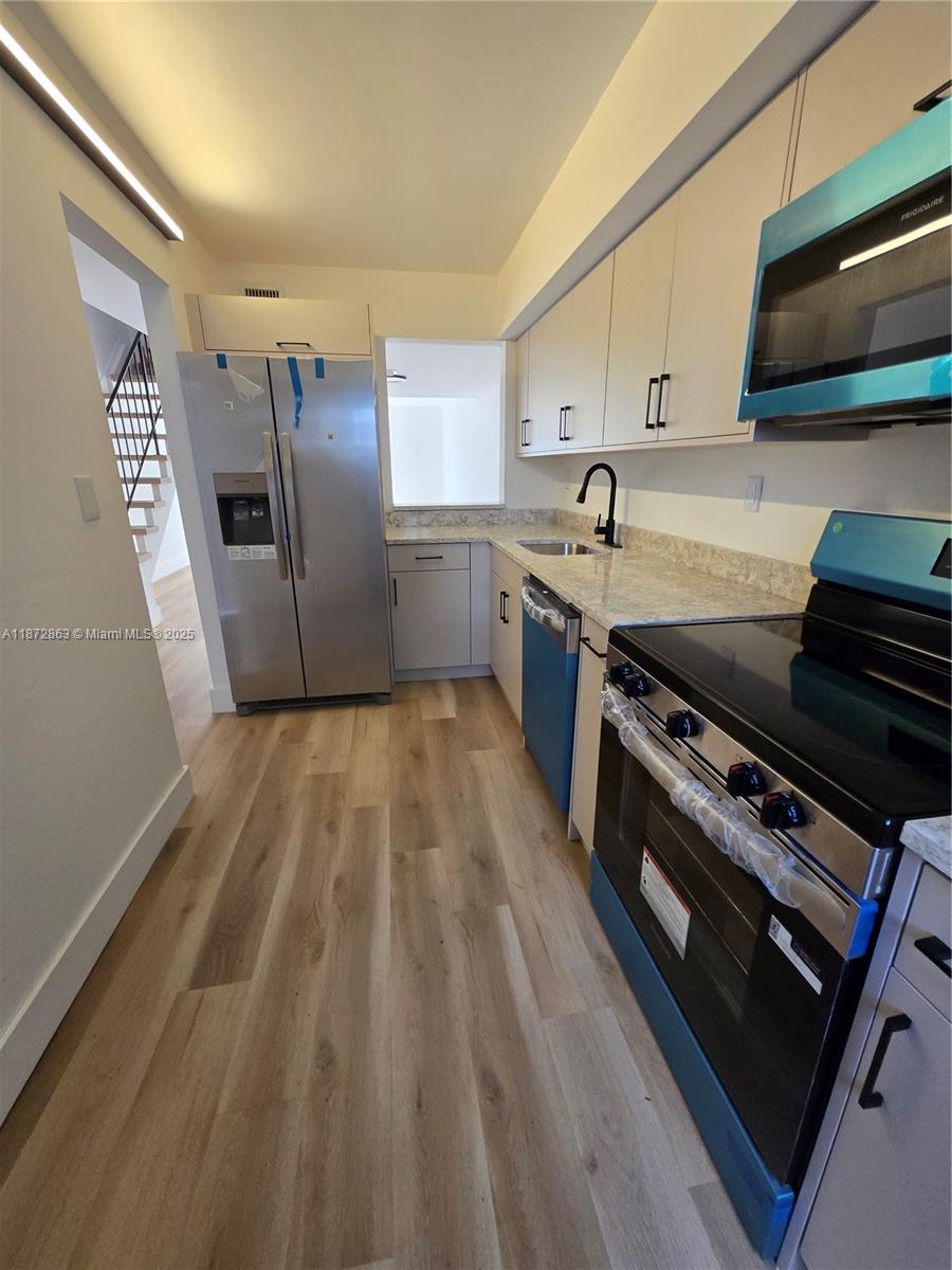 A modern kitchen features light wood-look flooring, stainless steel appliances, and white cabinetry — 15124 SW 81st St # 102, Miami FL 33193, MIAMI, FL