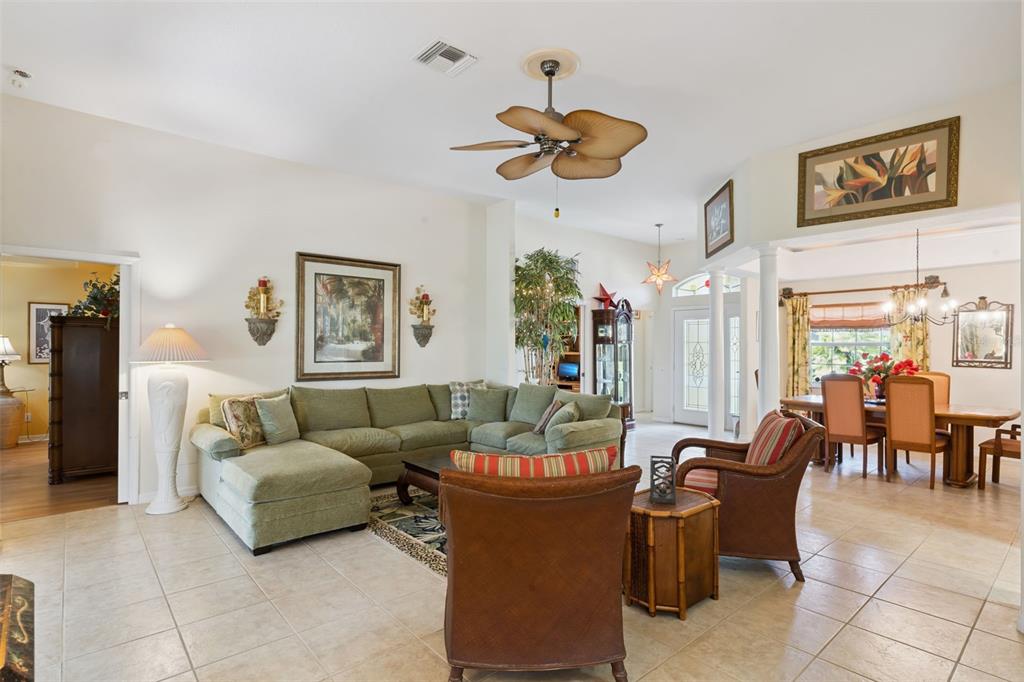 A spacious living room features a green sectional sofa, tiled floors, and a ceiling fan — 21325 ROYAL TROON DRIVE, LEESBURG, FL