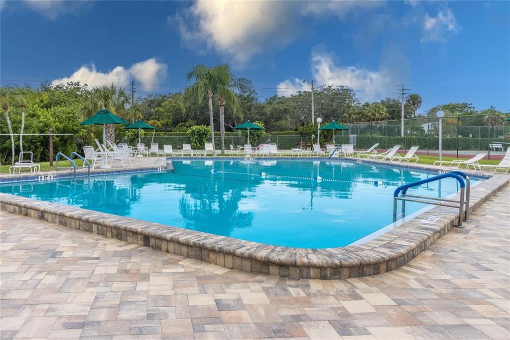 An outdoor swimming pool with a stone paver deck, lounge chairs, and umbrellas — 1435 57TH STREET W UNIT 1435, BRADENTON, FL
