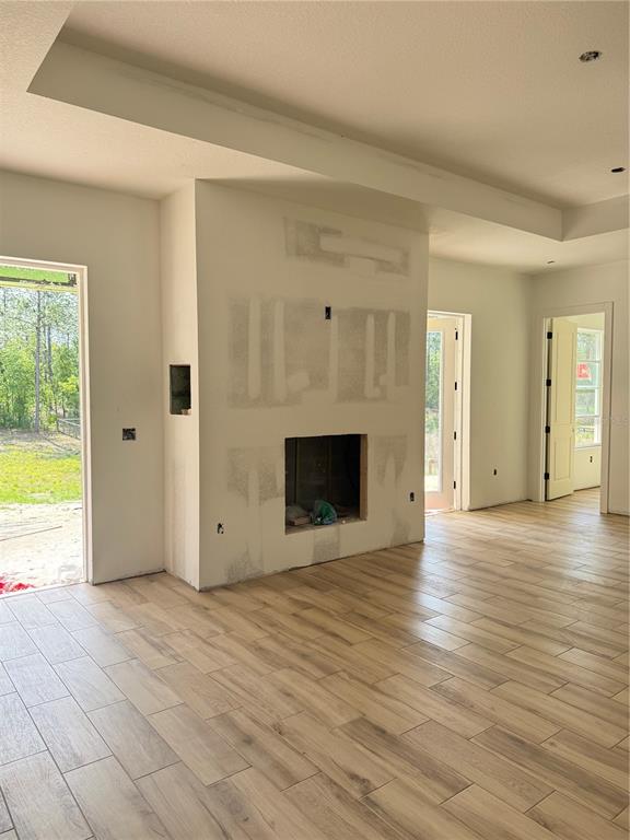 An unfinished living room features a fireplace, wood-look tile flooring, and views of the outdoors — 13989 SW 89TH STREET, DUNNELLON, FL