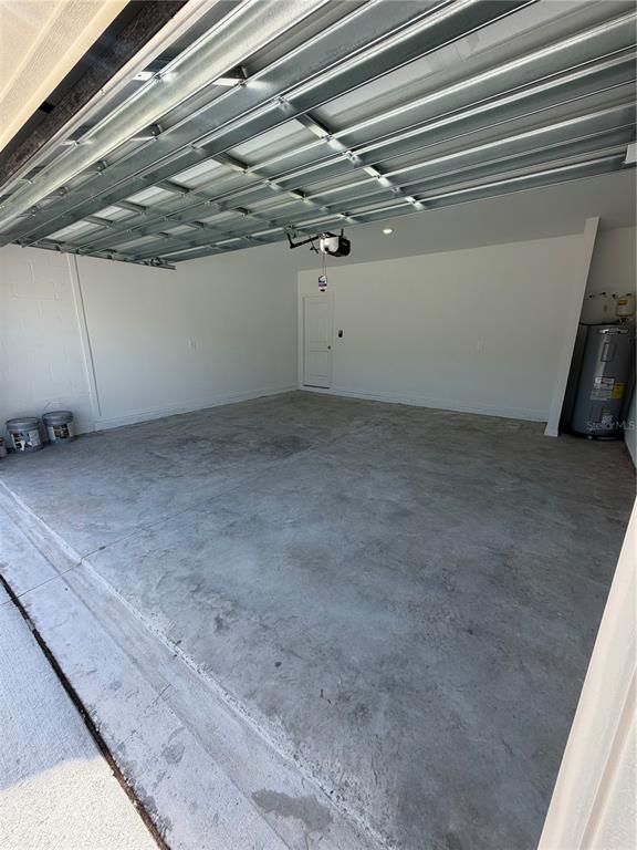 An empty garage features a concrete floor, white walls, and a metal roll-up door — 6468 DOMIZIO DRIVE, WINTER HAVEN, FL
