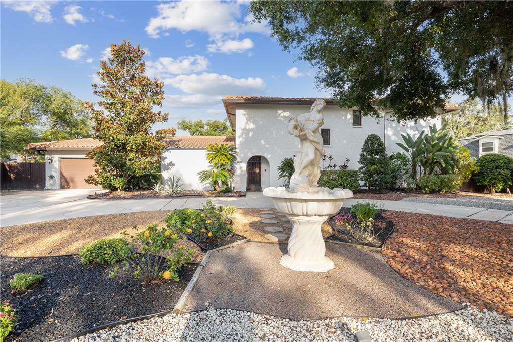 A white two-story house features a circular driveway, a large fountain, and landscaped garden beds — 403 WEEBURN ROAD, TEMPLE TERRACE, FL