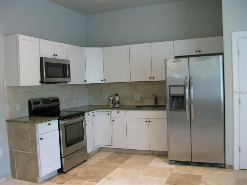A kitchen features white cabinets, stainless steel appliances, granite countertops, and light-colored tile flooring — 2009 COCOANUT AVENUE UNIT 2, SARASOTA, FL