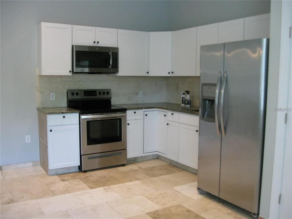 A kitchen features white cabinets, stainless steel appliances, granite countertops, and light-colored tile flooring — 2009 COCOANUT AVENUE UNIT 2, SARASOTA, FL