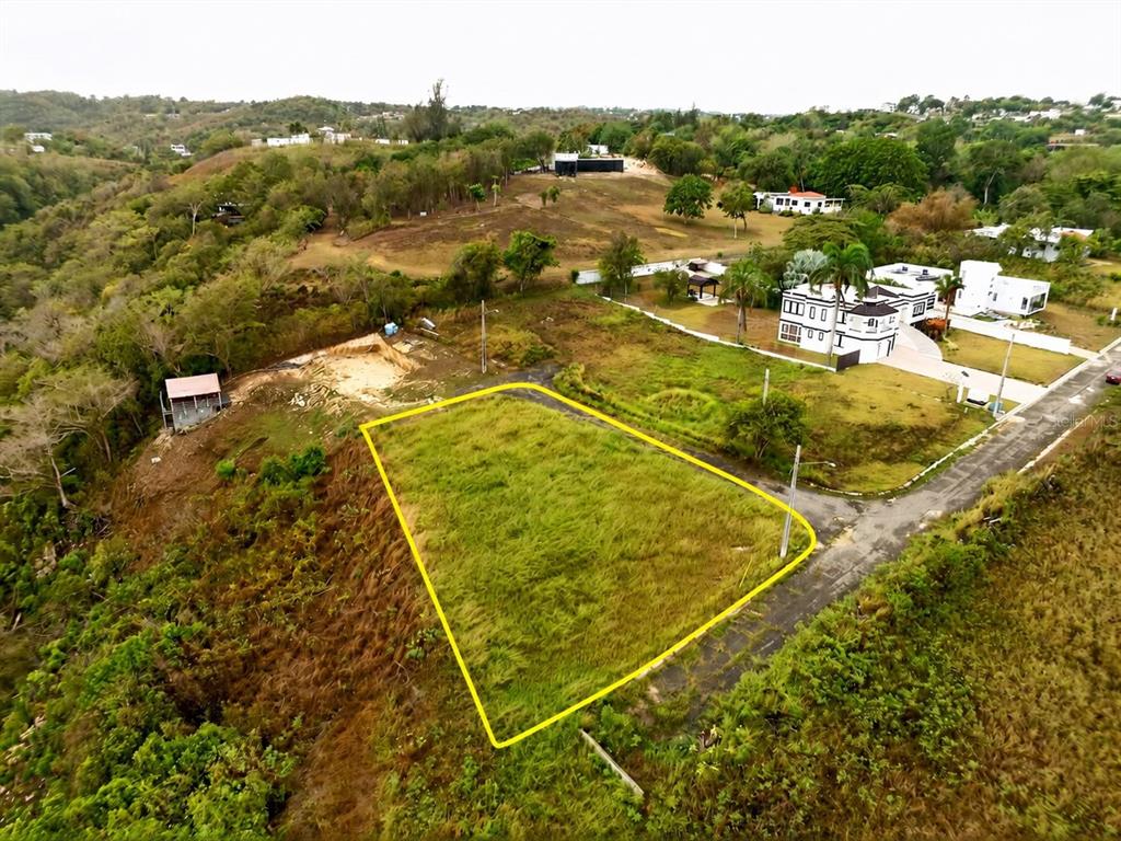An aerial view shows a vacant, grass-covered lot outlined in yellow next to a paved road — Carr. 485 Km HM. 1.5 BO. SAN JOSE SOLAR #8, QUEBRADILLAS, PR