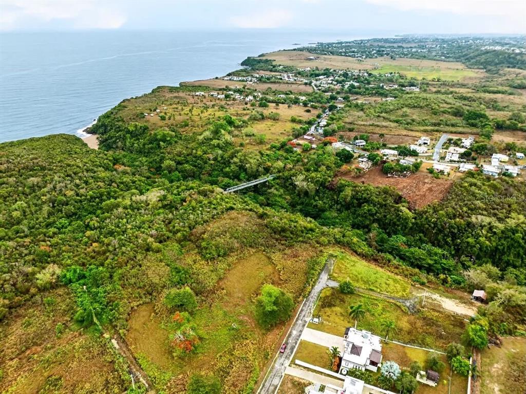 An aerial view shows a coastal landscape with a bridge spanning a forested ravine — Carr. 485 Km HM. 1.5 BO. SAN JOSE SOLAR #8, QUEBRADILLAS, PR