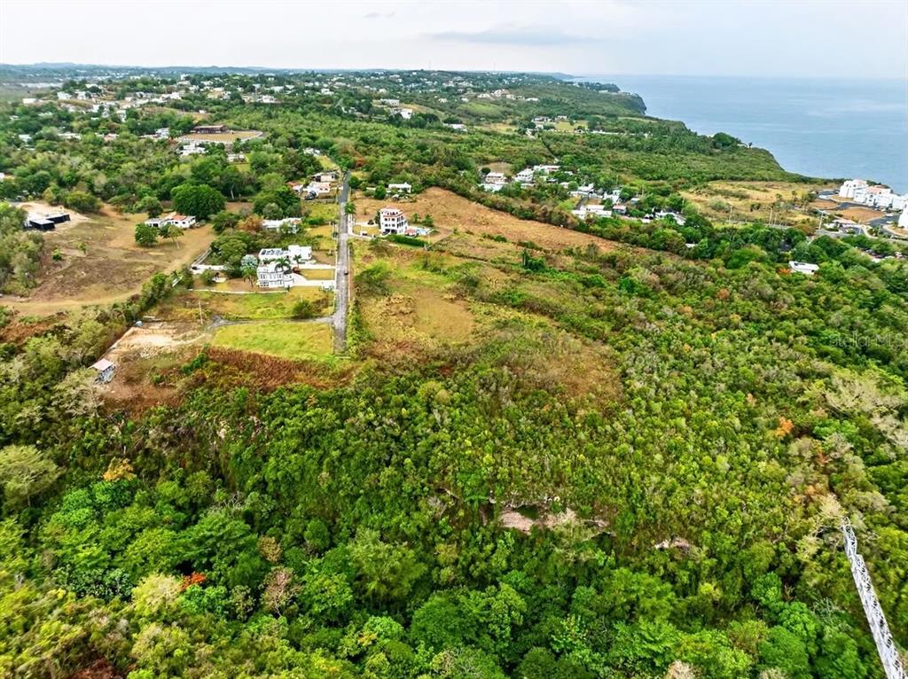 An aerial view shows a coastal landscape with scattered houses, a road, and dense vegetation — Carr. 485 Km HM. 1.5 BO. SAN JOSE SOLAR #8, QUEBRADILLAS, PR